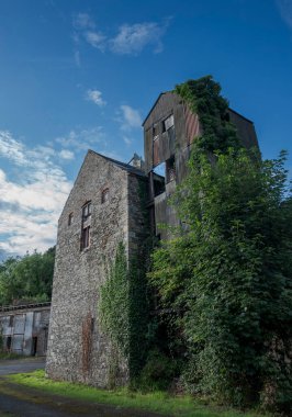 Yıkılmış kule asbest kaplı çatı çarşafları ve sarmaşıkla kaplanmış. Yıpranmış, çökmüş duvarları ihmal ve endüstriyel bozulmayı yansıtıyor. Fotoğraf Inniskeen, County Monaghan, İrlanda 'da çekildi.