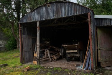 Inside the dark, neglected shed, disordered wooden planks and a dumper are piled haphazardly, surrounded by dirt and dust. Photo taken in Inniskeen, County Monaghan, Ireland clipart