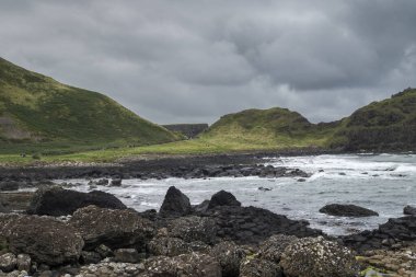 Kuzey İrlanda 'daki Giant' s Causeway yakınlarında Antrim Sahili boyunca uzanan siyah bazalt çakıl taşı plajından sakin bir manzara. Ufuk bulutlu bir gökyüzünün altında okyanus boyunca uzanıyor..
