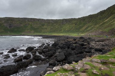 Kuzey İrlanda 'daki Giant' s Causeway yakınlarında Antrim Sahili boyunca uzanan siyah bazalt çakıl taşı plajından sakin bir manzara. Ufuk bulutlu bir gökyüzünün altında okyanus boyunca uzanıyor..