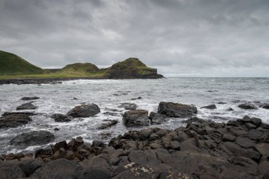 Kuzey İrlanda 'daki Giant' s Causeway yakınlarında Antrim Sahili boyunca uzanan siyah bazalt çakıl taşı plajından sakin bir manzara. Ufuk bulutlu bir gökyüzünün altında okyanus boyunca uzanıyor..