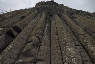 İrlanda 'nın Giant' s Causeway kentindeki kayalık duvarda bulutlu gökyüzünün altında doğal jeolojik oluşumları gösteren bazalt sütunlar bulunuyor.