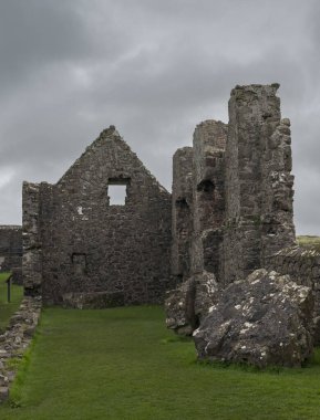 Kuzey İrlanda 'daki Dunluce Şatosu' nun kalıntıları. Bulutlu gökyüzünün altında duran taş duvarları ve kuleleri ortaçağ mimarisini aydınlatıyor..
