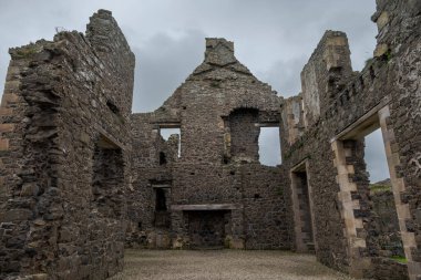 Kuzey İrlanda 'daki Dunluce Şatosu' nun kalıntıları. Bulutlu gökyüzünün altında duran taş duvarları ve kuleleri ortaçağ mimarisini aydınlatıyor..