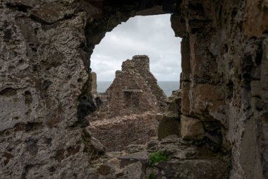 Ruins of Dunluce Castle in Northern Ireland, with the remains of its stone walls and towers standing under a cloudy sky, highlighting its medieval architecture. clipart