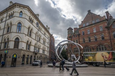 BELFAST, NORTHERN IRELAND - 4 AĞUSTOS 2023: Arthur Meydanı, çağdaş sanatı bulutlu bir gökyüzü altında klasik mimariyle harmanlayan, tarihi binalarla çevrili, modern dairesel bir heykele sahiptir.