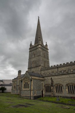 Saint Columb Cathedral with a Gothic spire and weathered gravestones under an overcast sky, Londonderry, Northern Ireland clipart