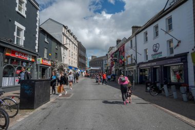 GALway, IRELAND - 6 AĞUSTOS 2023: Galway, İrlanda 'da küçük dükkanlar ve yayaların yer aldığı hareketli bir cadde, parçalı bulutlu bir gökyüzünün altında kaldırımlarda geziniyor.