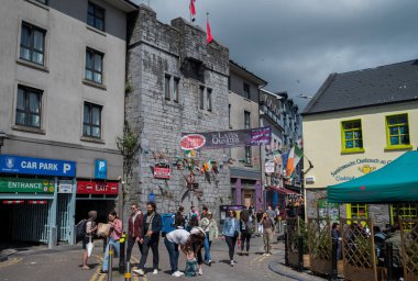 GALway, IRELAND - 6 Ağustos 2023: Galway, İrlanda 'nın Latin Mahallesi' nde canlı bir cadde, tarihi taş binalar, renkli dükkanlar ve parçalı bulutlu bir gökyüzünün altında yürüyen insanlar