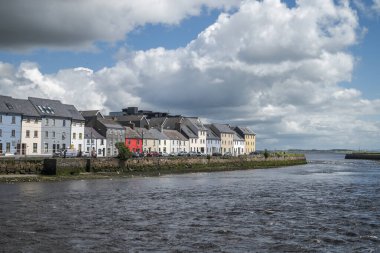 GALway, IRELAND - 6 AĞUSTOS 2023: Parçalı bulutlu bir gökyüzünün altında Galway, İrlanda 'da bir nehir kıyısı boyunca çok renkli evler dizisi