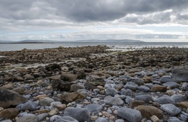 Silverstrand Sahili 'ndeki kayalık kıyı şeridi, Galway, İrlanda, sakin deniz ve bulutlu gökyüzü