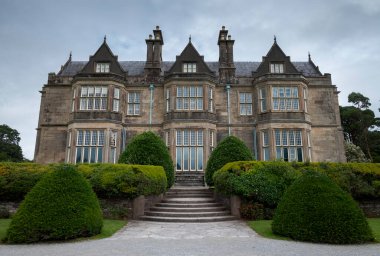 COUNTY KERRY, IRELAND - 8 AĞUSTOS 2023: Muckross Malikanesi, bulutlu bir gökyüzü altında taş basamaklar ve budanmış çalıları içeren zarif Viktorya dönemi mimarisini sergiliyor