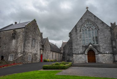 Adare, İrlanda 'daki Trinitarian Manastırı' nda, bulutlu bir gökyüzünün altında sivri kemerli bir pencere ve kırmızı bir kapı bulunur..