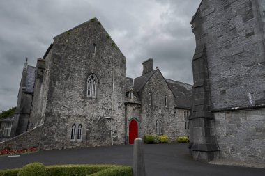 Adare, İrlanda 'daki Trinitarian Manastırı' nda yemyeşil yemyeşil bir gökyüzü ile çevrili çarpıcı kırmızı bir kapı ve gotik bir mimari yer alıyor.