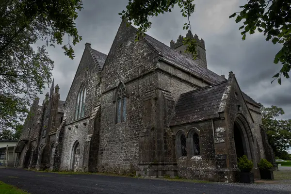 Adare Friary, İrlanda, sivri kemerli mimarisi olan eski bir taş bina, çok katlı çatılar, ve bulutlu bir gökyüzüne karşı kurulmuş görünür bir çan kulesi.