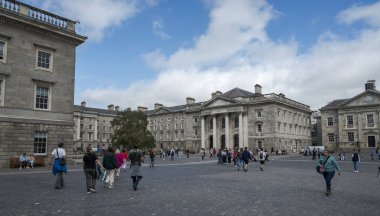 DUBLIN, IRELAND - 10 AĞUSTOS 2023: Trinity Koleji 'nde yürüyen insanların bulunduğu klasik mimari binalarla çevrili kaldırımlı geniş bir avlu