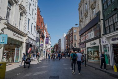DUBLIN, IRELAND - 10 Ağustos 2023 Dublin 'de yayalar, canlı mağazalar ve tarihi binalarla dolu hareketli bir alışveriş caddesi. Sahnede sokak satıcıları, renkli tabelalar ve açık bir gökyüzünün altında yürüyen insanlar yer alıyor.