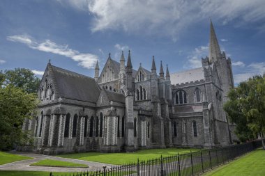 Dublin, İrlanda 'daki St. Patrick Katedrali, bulutlu mavi bir gökyüzünün altında. Gotik mimarisi ve taş yapısı yeşilliğin ortasında göze çarpıyor..