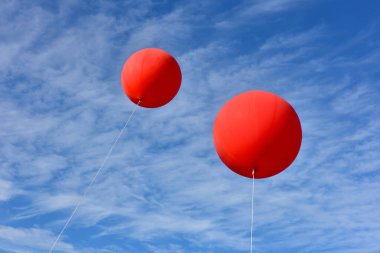 Kırmızı balonlar. Devasa bir şişme kırmızı reklam balonu güneşli mavi gökyüzünde süzülüyor..