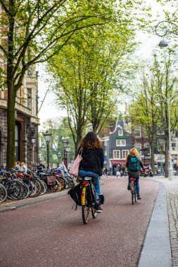 AMSTERDAM, NETHERLANDS - 27 Eylül 2017: Amsterdam Şehir Merkezi 'nde bisiklet süren insanlar. Köprü ve tipik Hollanda evleriyle Amsterdam caddesinin güzel manzarası. Amsterdam, Hollanda