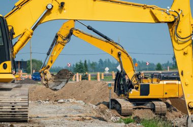 İki sarı kazıcı bir yol inşaatında çalışıyor. Arka planda yol işaretleri var, çerçeve etkisi var.