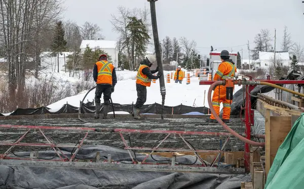İşçiler beton pompayla beton dökerek bir levha yapıyorlar, kış.