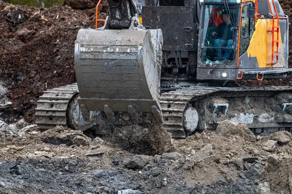 Kazı kovası yakın çekimde, toprak dökülüyor.