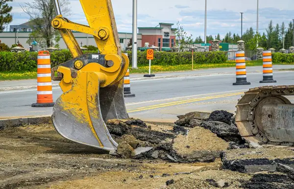 Sarı kazıcı kovası yol inşaatında asfalt topluyor.