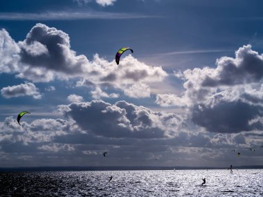 Backlit silhouettes of many kitesurfers surfing on the sea, Jastarnia, Poland