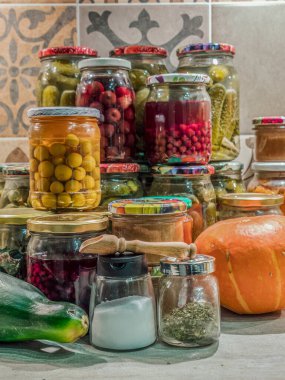 Mutfak masasının üstüne istiflenmiş kavanozlarda çeşitli meyve ve sebze konserveleri.