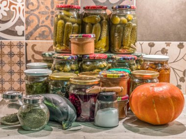 Mutfak masasının üstüne istiflenmiş kavanozlarda çeşitli meyve ve sebze konserveleri.