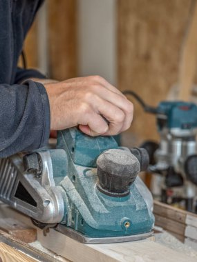 Marangoz elektrikli bir el planörüyle tahta dikiyor.