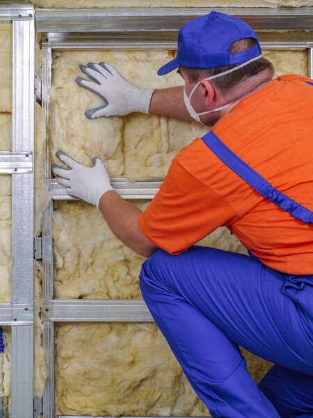 Construction worker thermally insulating house attic with mineral wool