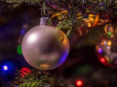 Sıcak ve renkli ışıkları yansıtan, bayram kutlamalarını ve neşeli anları sembolize eden Noel ağacı süsü. Odaklanmış kompozisyon, Noel mevsiminin sihrini ve sıcaklığını çağrıştırıyor.