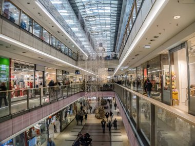 Tatil ışıkları ve süslemelerle donatılmış, çeşitli perakende mağazalarına göz atarken neşeli ortamın tadını çıkaran müşterilerle dolu, hareketli bir alışveriş merkezi.