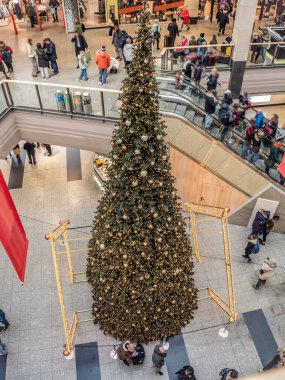 Tatil sezonunda alışveriş merkezinde süslerle süslenmiş büyük bir Noel ağacı, alışveriş merdiveni üzerinde müşterilerle neşe ve şenlik ruhunu yakalıyor.