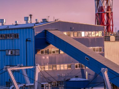 A large industrial plant featuring a prominent smokestack, surrounded by buildings and pipelines, photographed during sunset with a captivating magenta and orange sky clipart