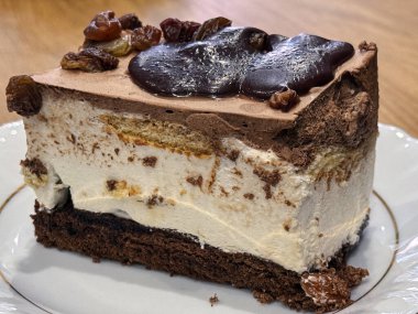 Üzüm ve sosla kaplı nefis bir dilim çikolata ve kremalı tatlı. Bir tabakta mükemmel bir şekilde sergilenen bu ikram, dokuların ve hoşgörülü tatların bir karışımını sergiliyor.