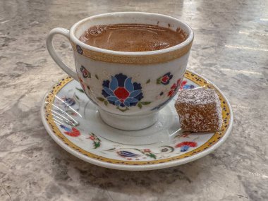 İçinde geleneksel Türk kahvesi bulunan güzel boyanmış bir fincanda, bir parça Türk lezzeti ayrıntılı bir dekoratif fincan üzerinde servis ediliyor.