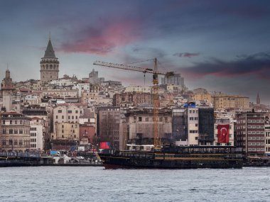 İstanbul 'un ikonik Galata Kulesi, yakındaki kentsel binalar ve İstanbul, Türkiye' deki yoğun bulut bulutları altındaki Boğaz sularını gösteren manzarası.