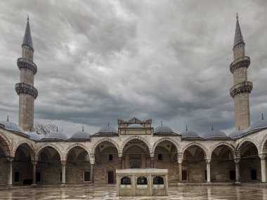 Yüksek minarelerle çevrili, dramatik bulutlu bir gökyüzü altında, yapının zengin kültürel ve tarihsel önemini yansıtan bir cami avlusunun karmaşık mimarisi., İstanbul, Türkiye