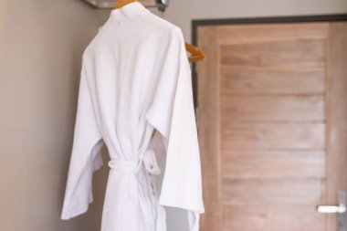 Taze ve temiz beyaz bornoz banyoda askıda asılı.