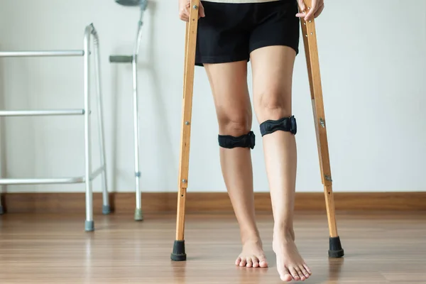 Patient women using knee support brace and crutches on white background