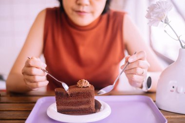 Kadın eli kaşık tutuyor ve masada lezzetli çikolatalı pasta yiyor.