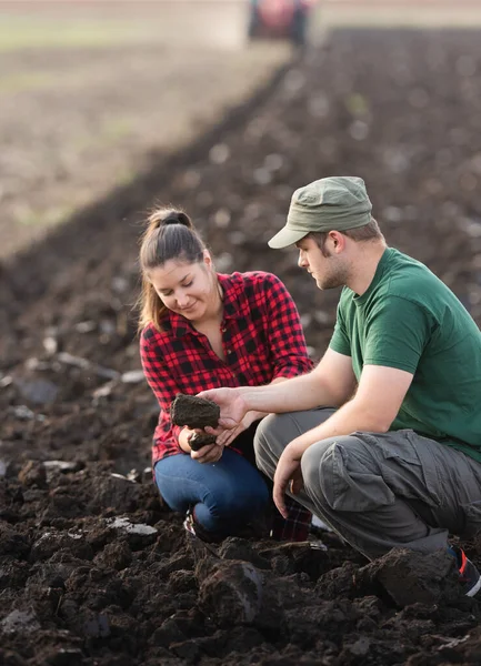 Young Farmers Examing Dirt While Tractor Plowing Field — Stock Photo, Image
