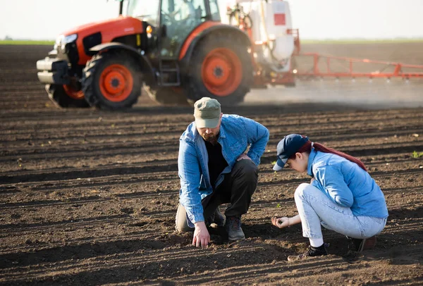 Giovani Agricoltori Che Esaminano Sporcizia Mentre Trattore Spruzza Campo — Foto Stock