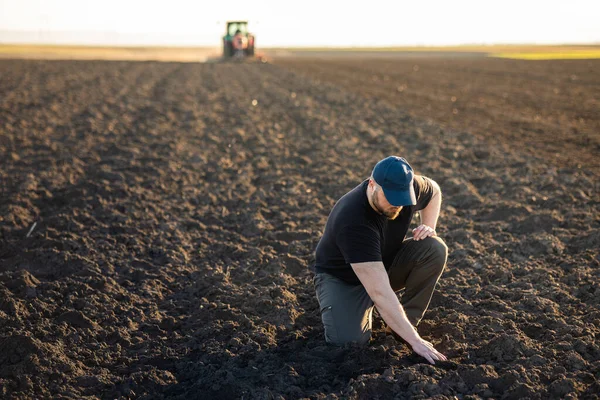 Young Farmer Examing Dirt While Tractor Plowing Field — Stock Photo, Image