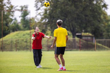 Genç bir kız, genç bir futbol oyuncusuna vurması için top fırlatıyor. - Ne? Bir erkek ve bir kız, güneşli bir günde Stadyumda antrenman yapıyorlar.