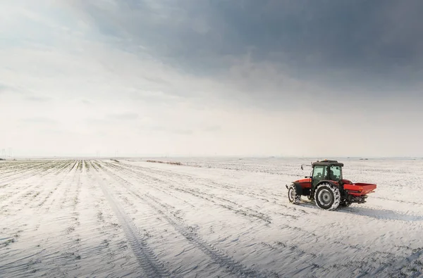 Farmer with tractor seeding - sowing crops at agricultural fields in winter - snow
