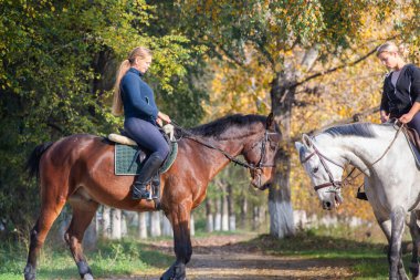Genç kızlar at sırtında orman yolunda